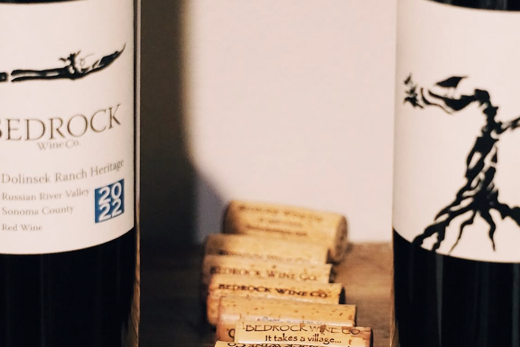Two Bedrock Wine Co. wine bottles with corks on a wooden surface.