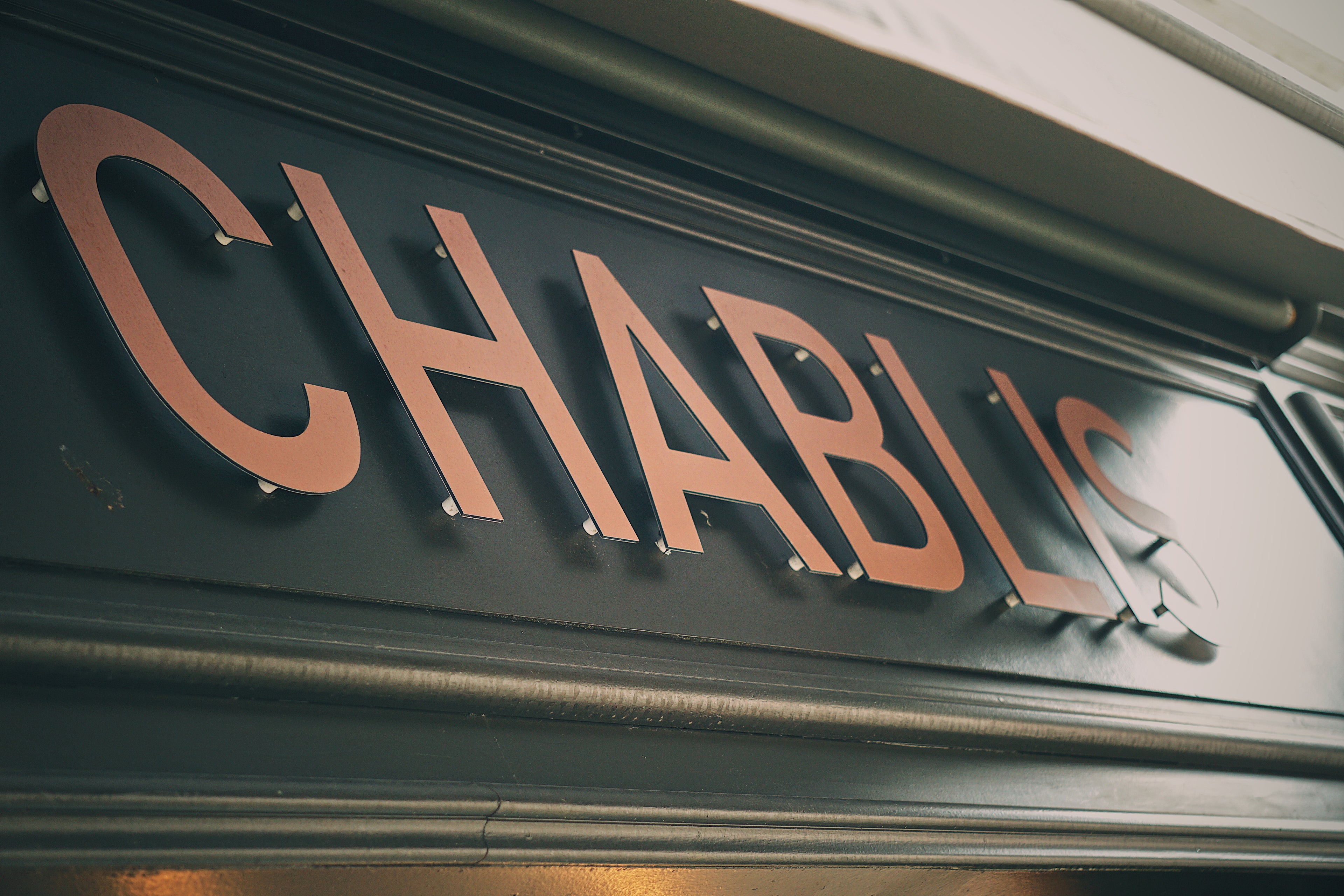 A stunning village sign for Chablis featuring raised gold lettering against a deep, dark teal background, captured during a journey through the heart of the Burgundy wine region.