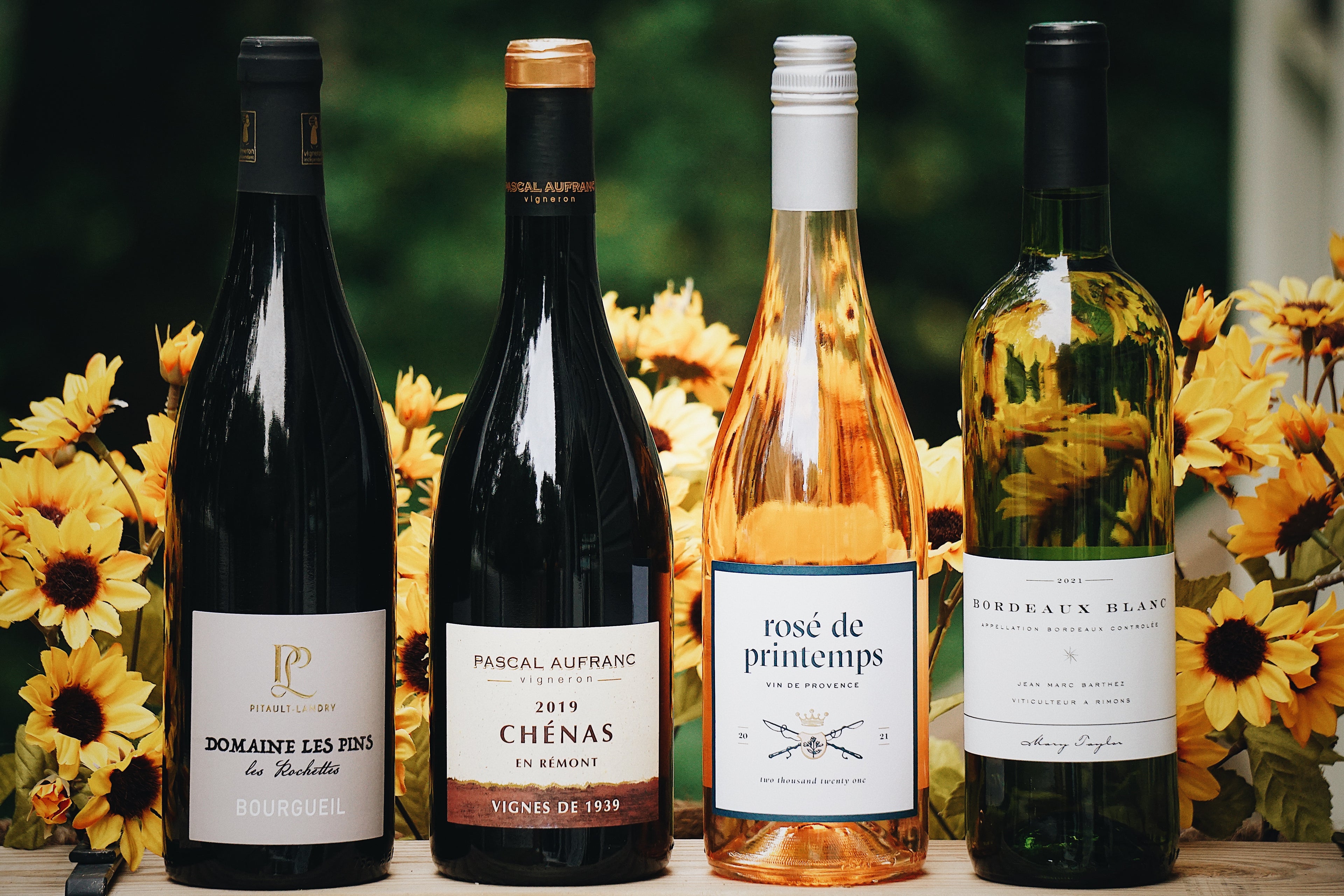 Four organic French wine bottles with labels in front of sunflower flowers