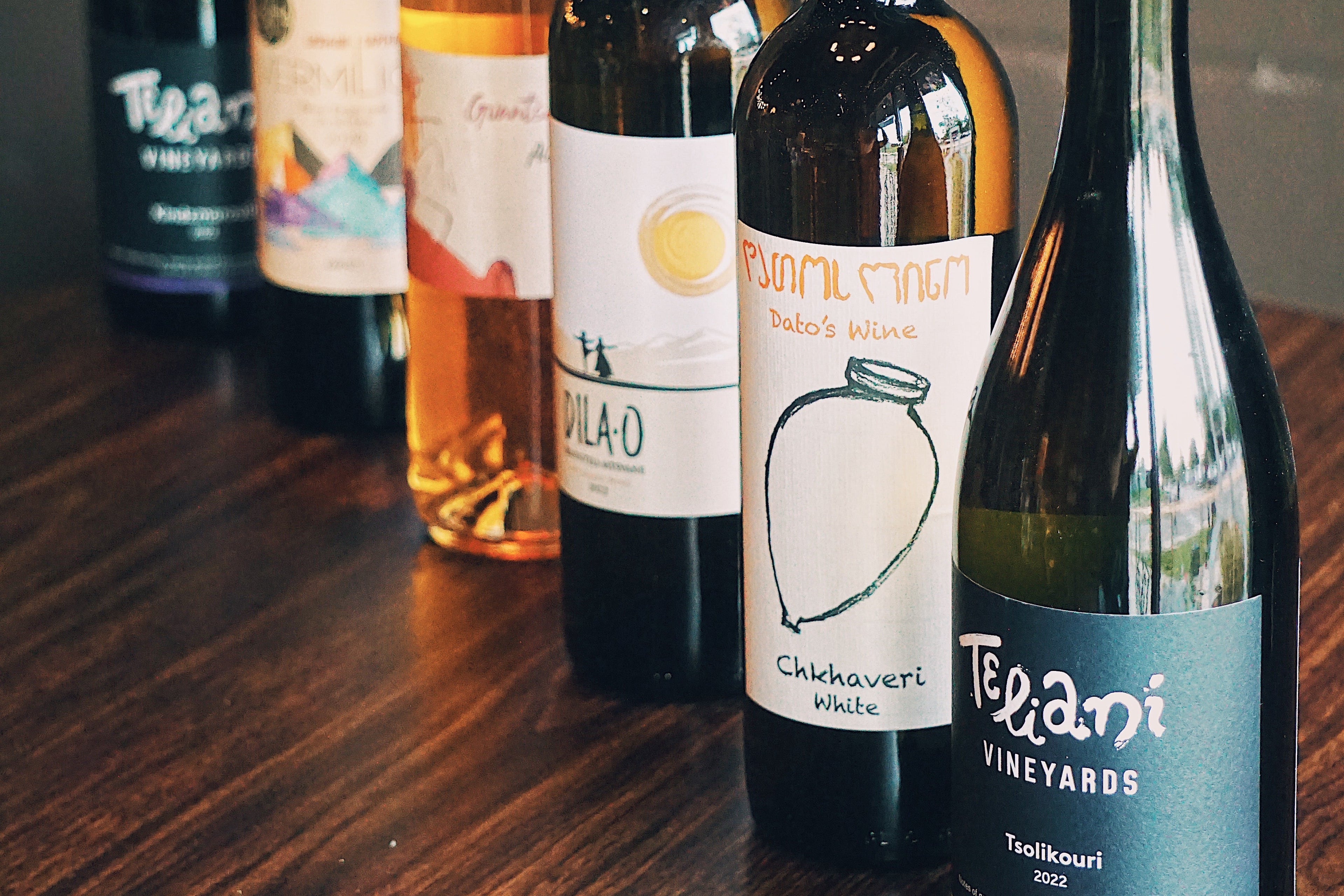 Collection of Georgian wine bottles on a wooden table with a brick wall background
