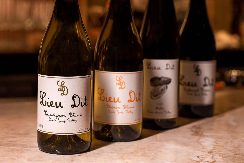 Four bottles of Lieu Dit wine on a bar counter with a blurred bar background.