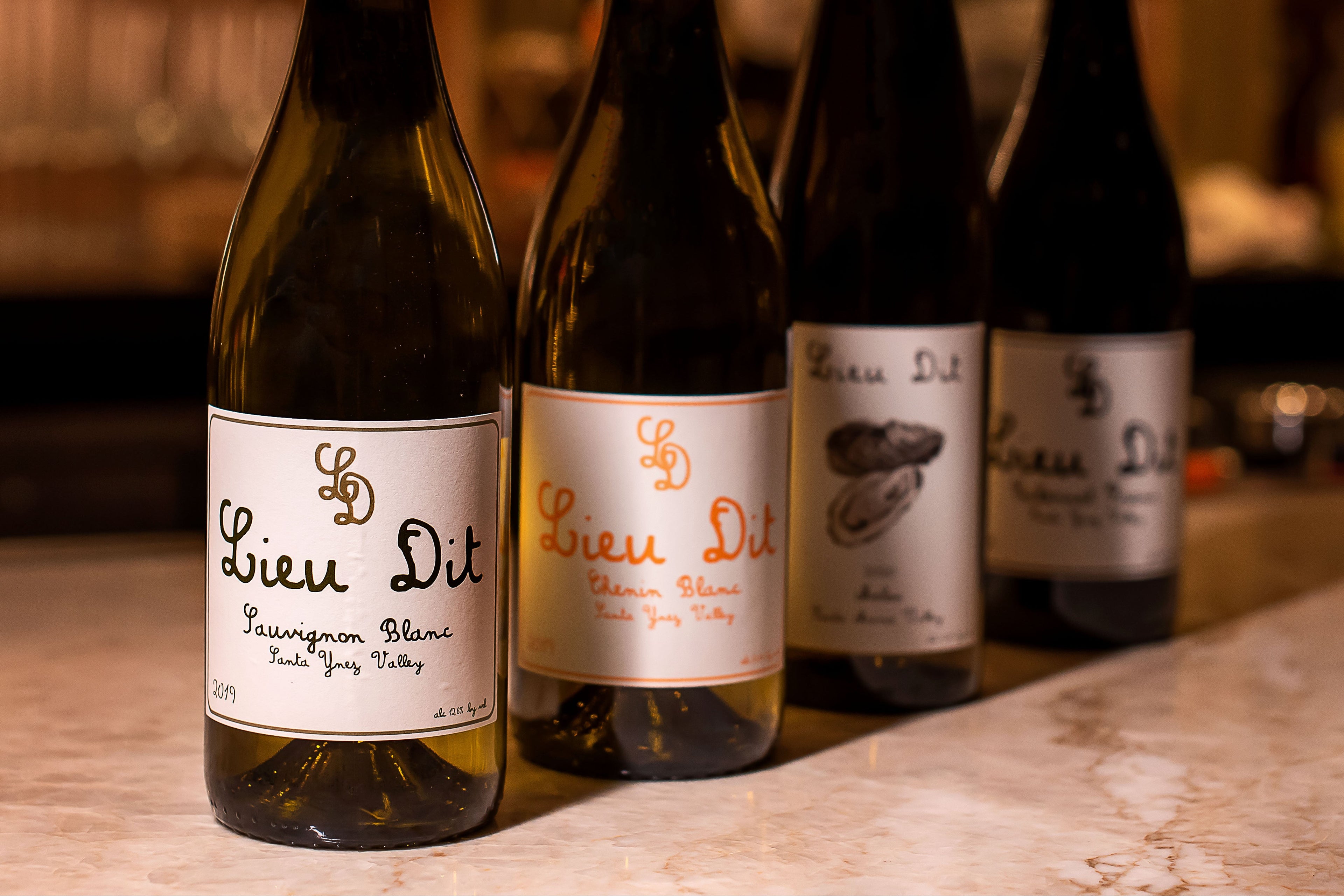 Four bottles of Lieu Dit wine on a bar counter with a blurred bar background.