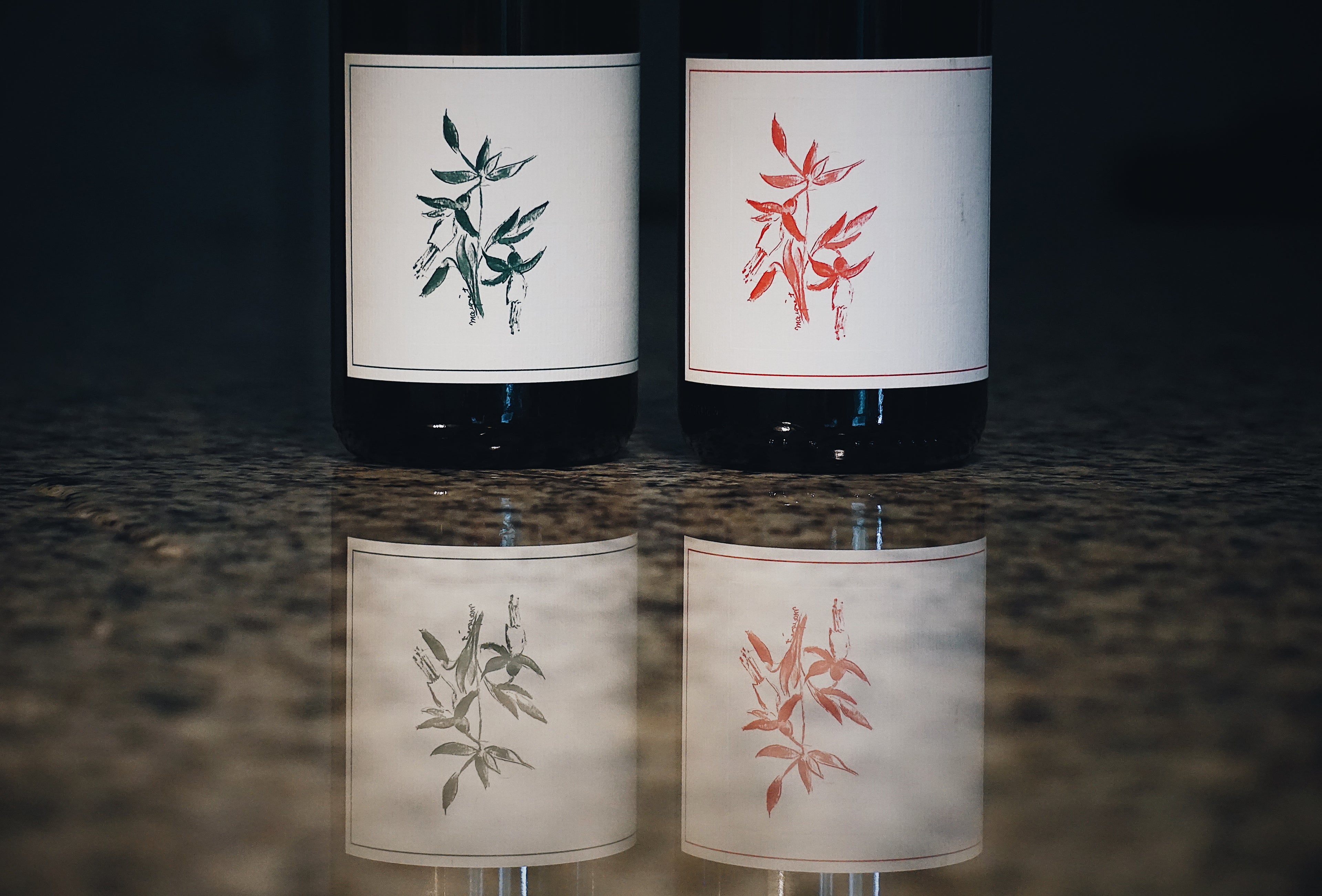 Two Arnot Roberts wine bottles with decorative labels featuring plant illustrations on a reflective surface.