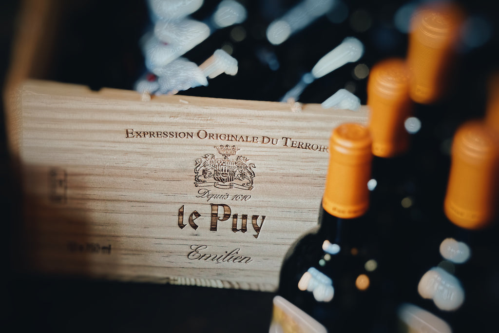 Wine bottles with a wooden box labeled 'le Puy' on a dark background
